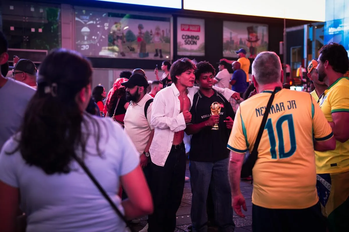 Brazilian fans gathering in Times Square at dusk, with a Neymar Jr jersey visible in the crowd and neon lights illuminating the scene