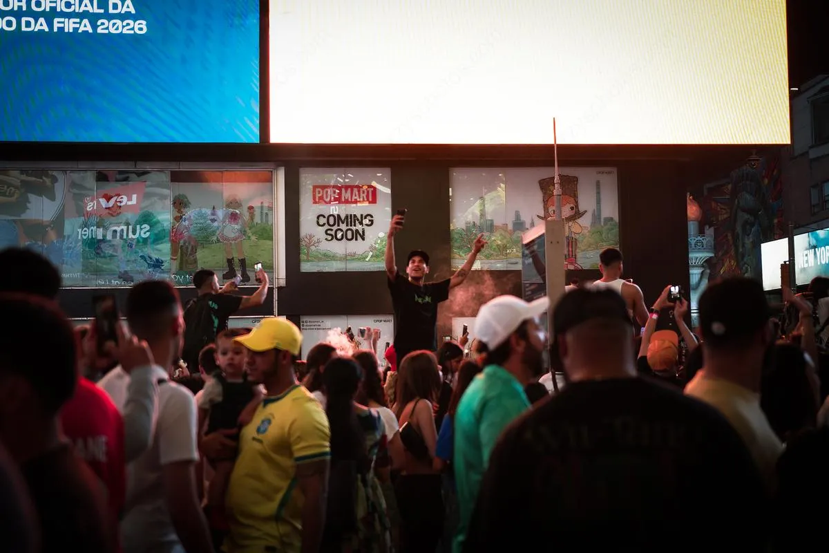Energetic fan standing on elevated position with arms raised, FIFA 2026 billboard and vibrant crowd below in Times Square
