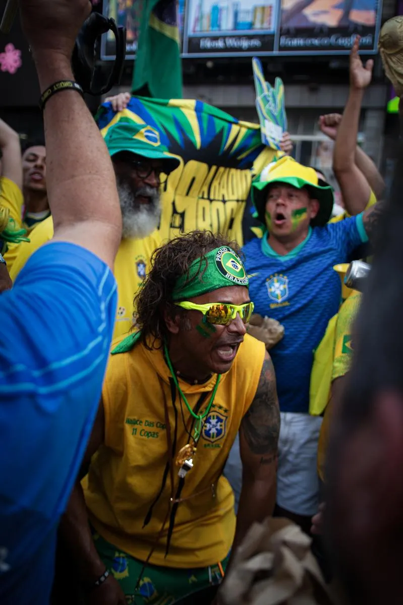 Passionate fan in yellow sleeveless shirt with Brazil headband and neon sunglasses shouting with arms raised, Brazilian flags waving behind