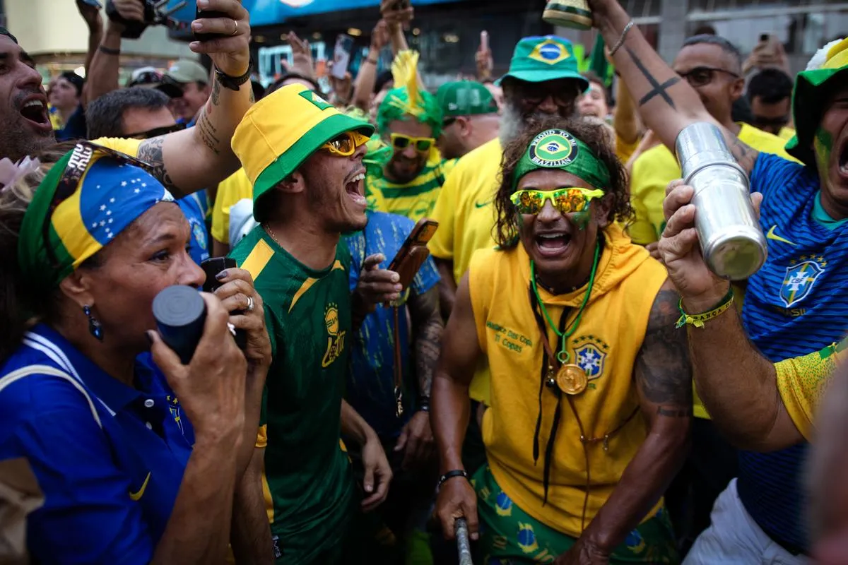 Intense celebration with fans screaming, woman drinking from cup with flag headwrap, men in yellow and green bucket hats cheering wildly