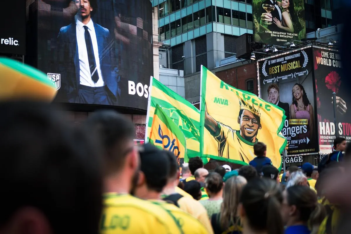 Pele tribute flag featuring crowned illustration waving above crowd in Times Square, Broadway billboards and Best Musical signs in background