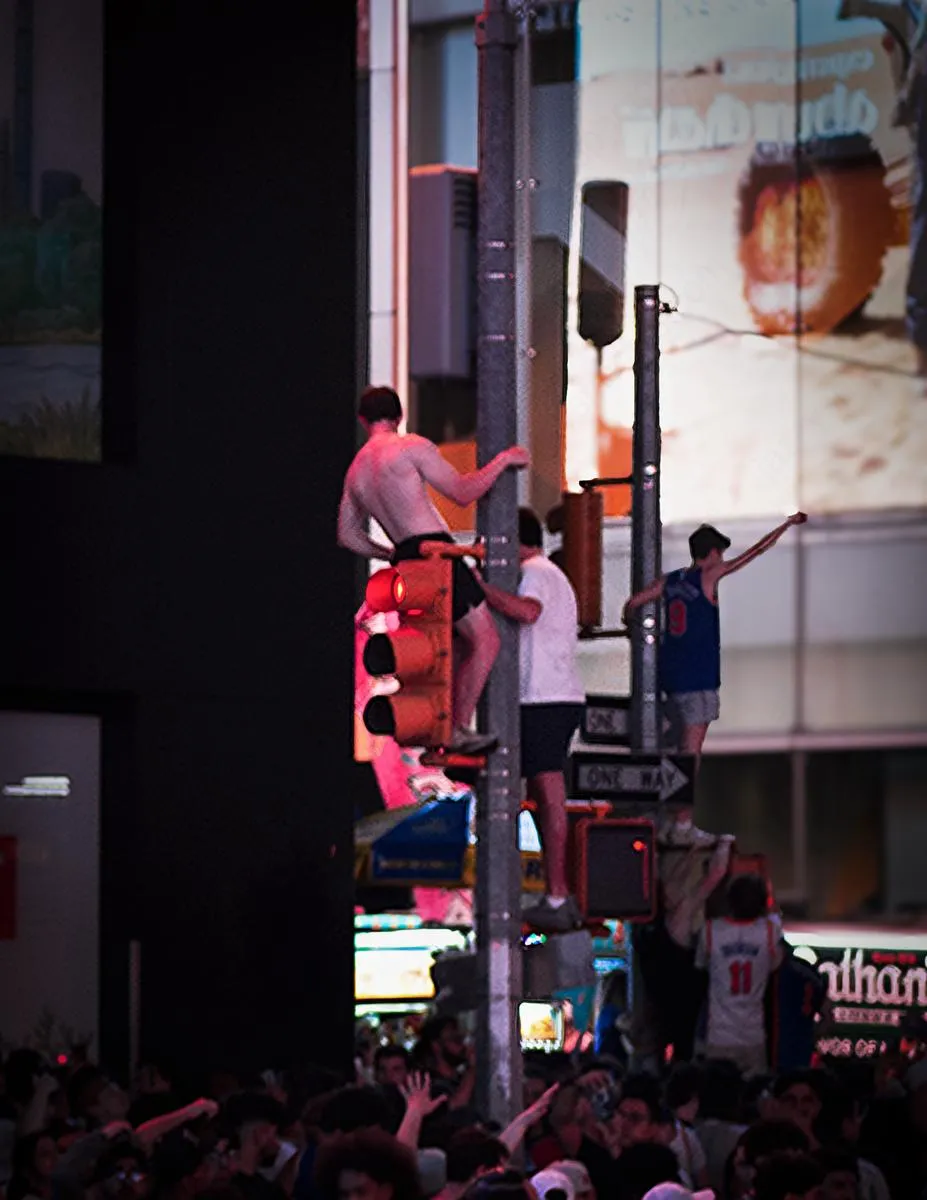 Fans climbing traffic light poles in Times Square at night with Knicks jerseys visible in the celebrating crowd below