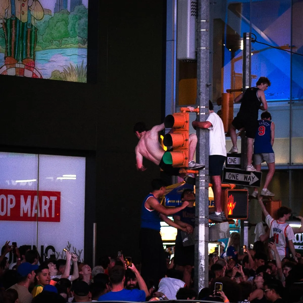 Multiple fans in Knicks jerseys climbing traffic lights and poles in Times Square celebration