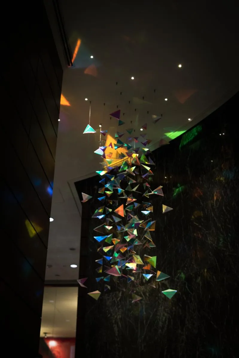 Colorful iridescent geometric sculpture installation with rainbow prisms hanging in dark space