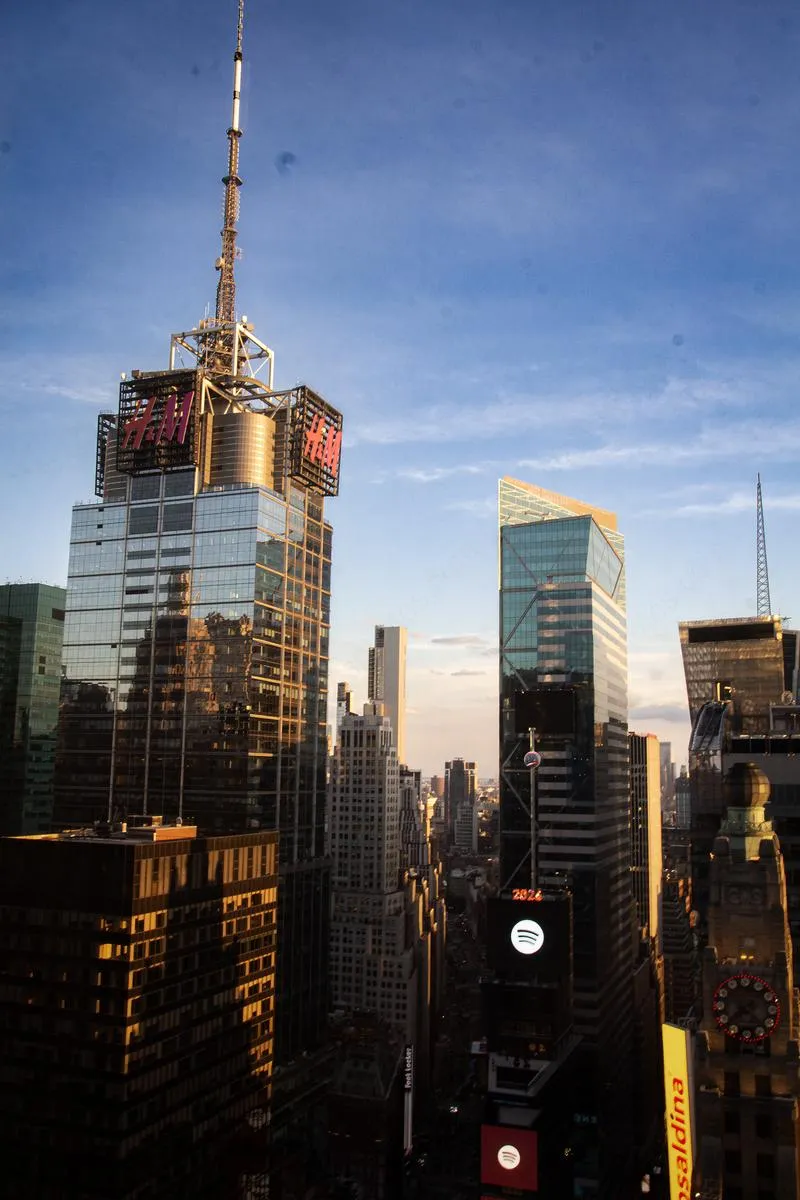 Manhattan skyline at golden hour with One Times Square tower and H&M sign visible from elevated viewpoint