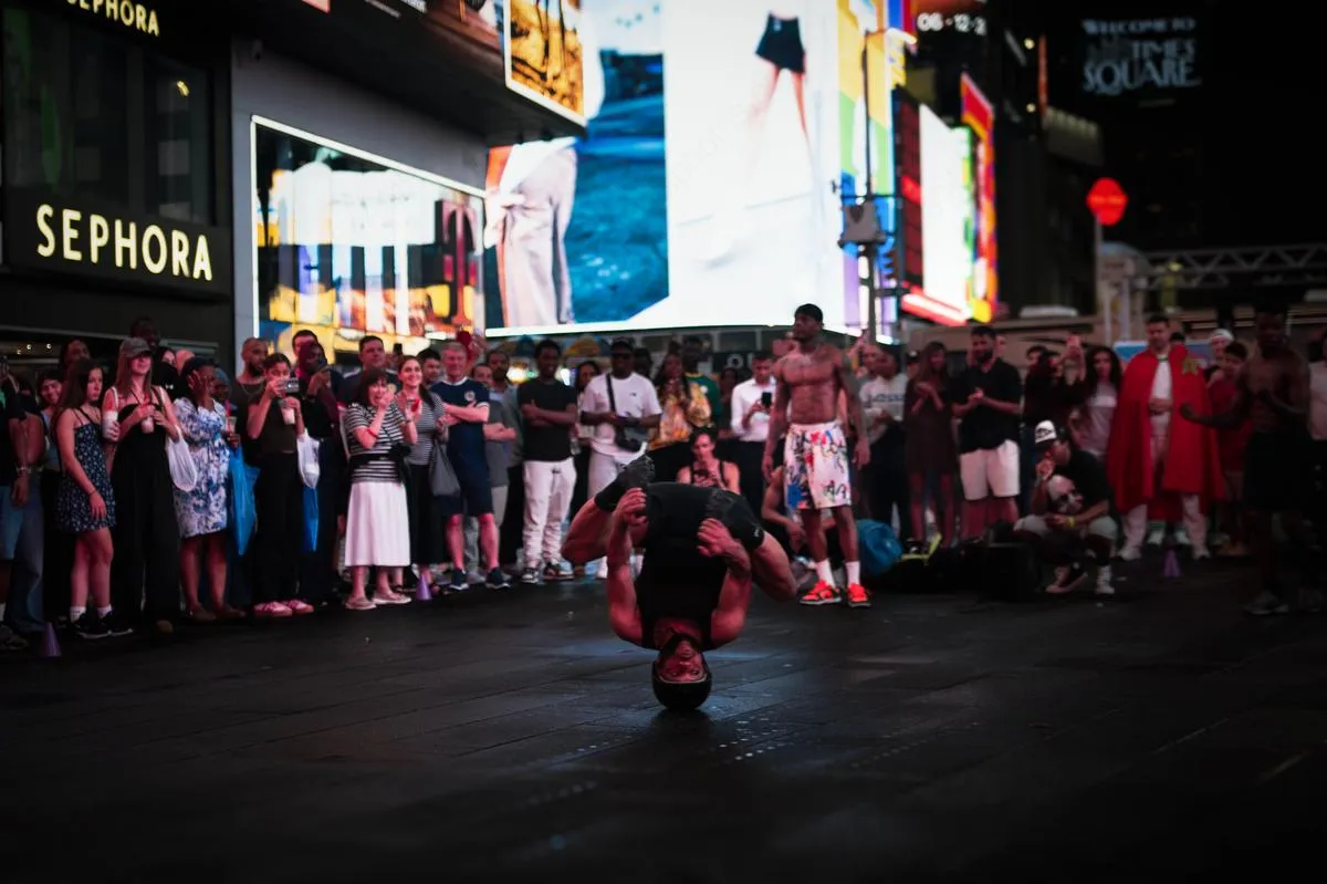 Breakdancer performing headstand freeze in Times Square with Sephora store and crowd watching behind him