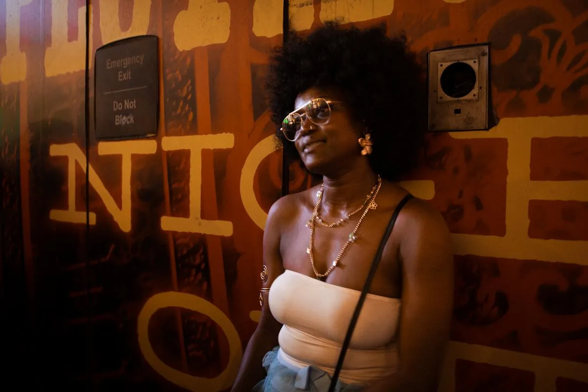 Stylish woman with natural afro hair and gold jewelry posing against orange graffiti wall at night