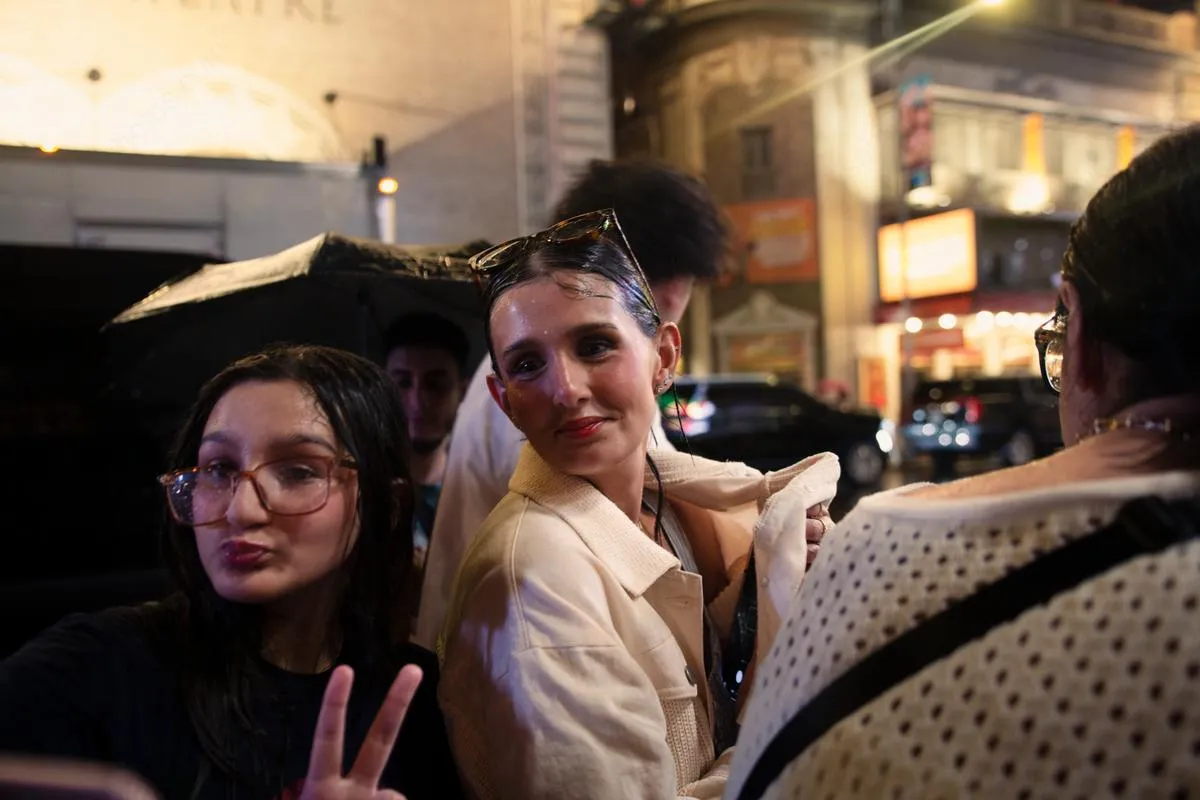 Young women smiling at camera with peace sign near Broadway theater district at night