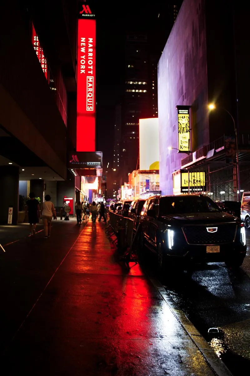 Rain-slicked street at night with Marriott Marquis neon sign glowing red and Lion King theater marquee visible