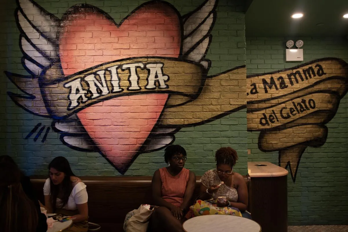 Women sitting in gelato shop beneath colorful Anita La Mamma del Gelato winged heart mural