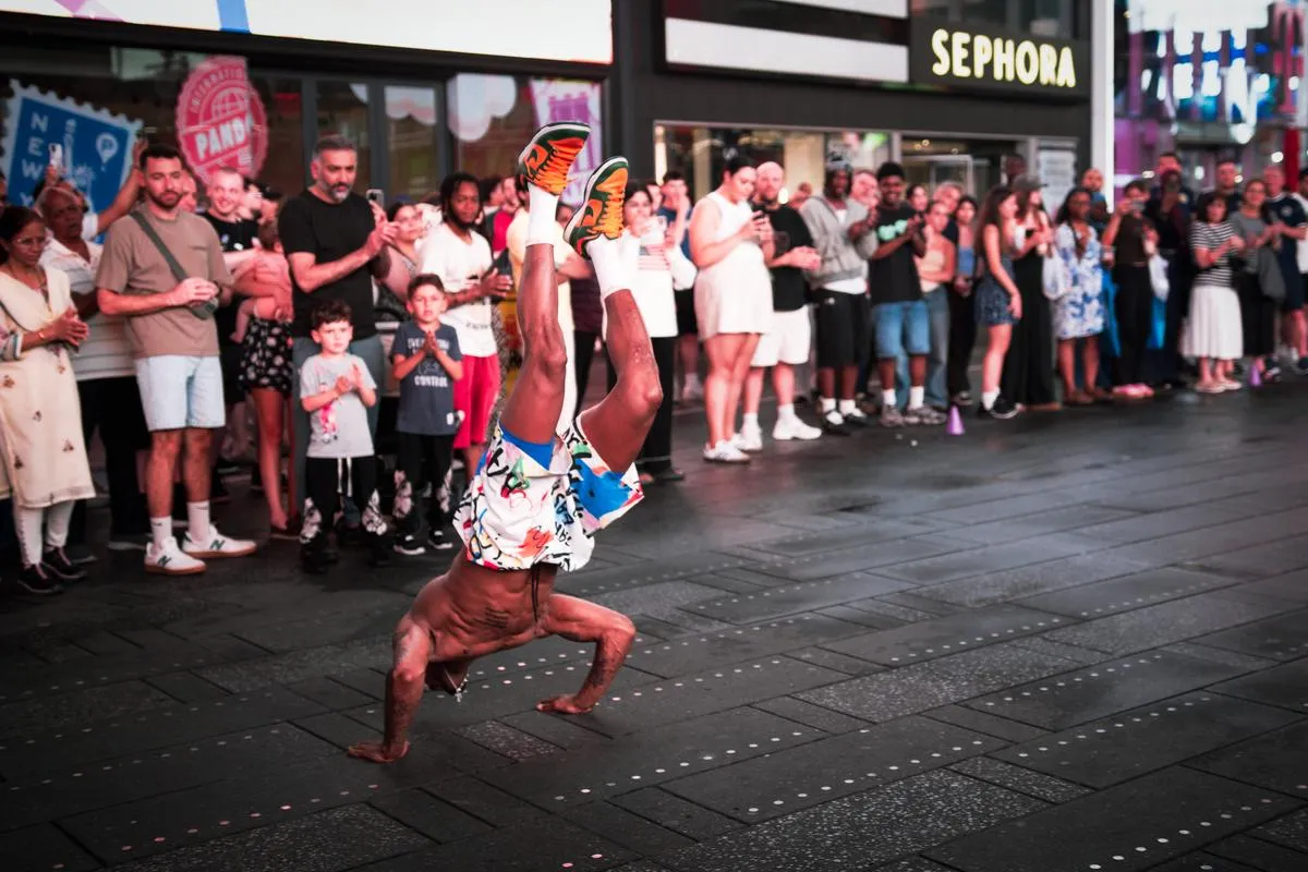 Breakdancer doing one-arm handstand with legs split in Times Square as diverse crowd watches
