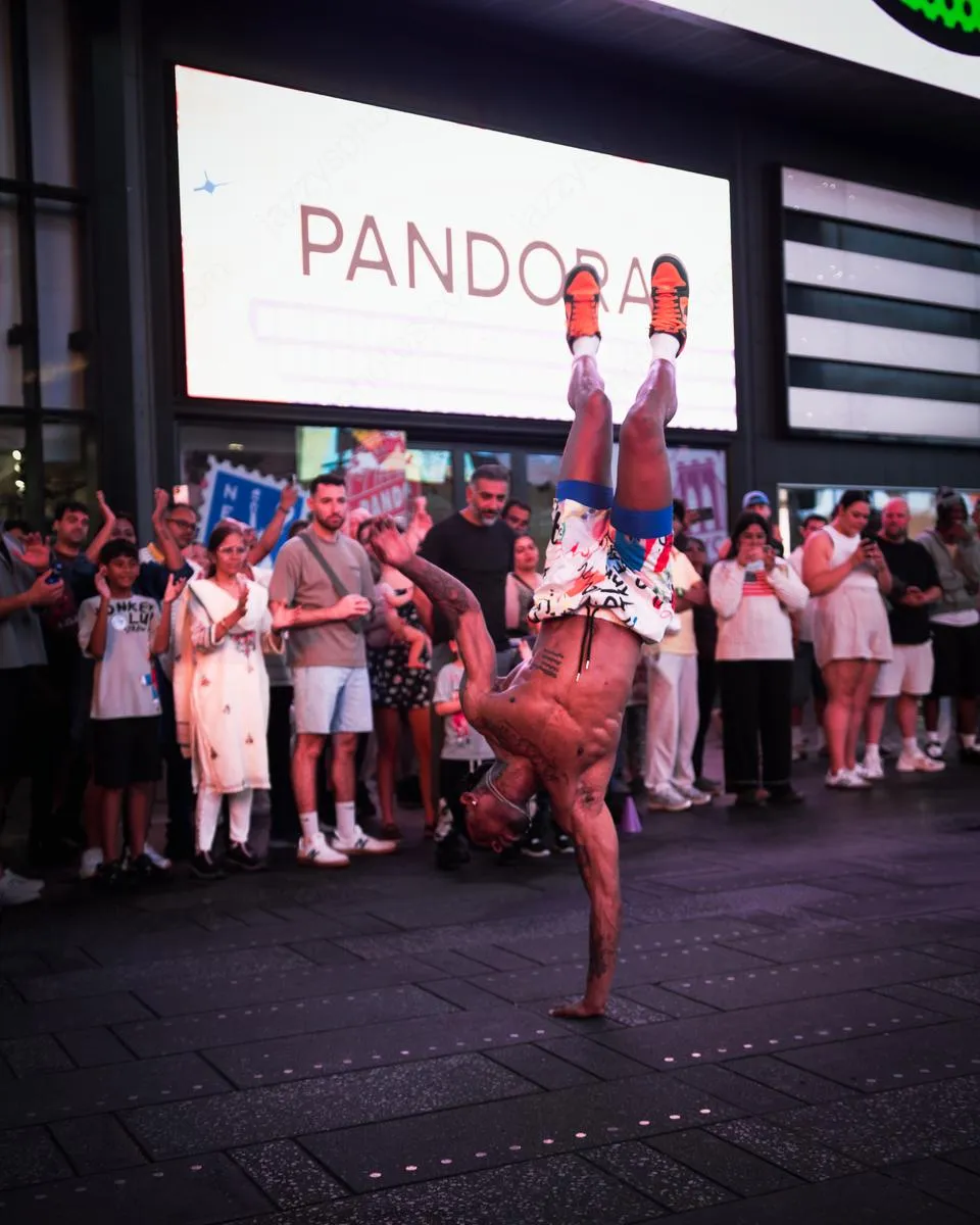 Muscular breakdancer performing one-arm handstand in front of Pandora store with crowd watching