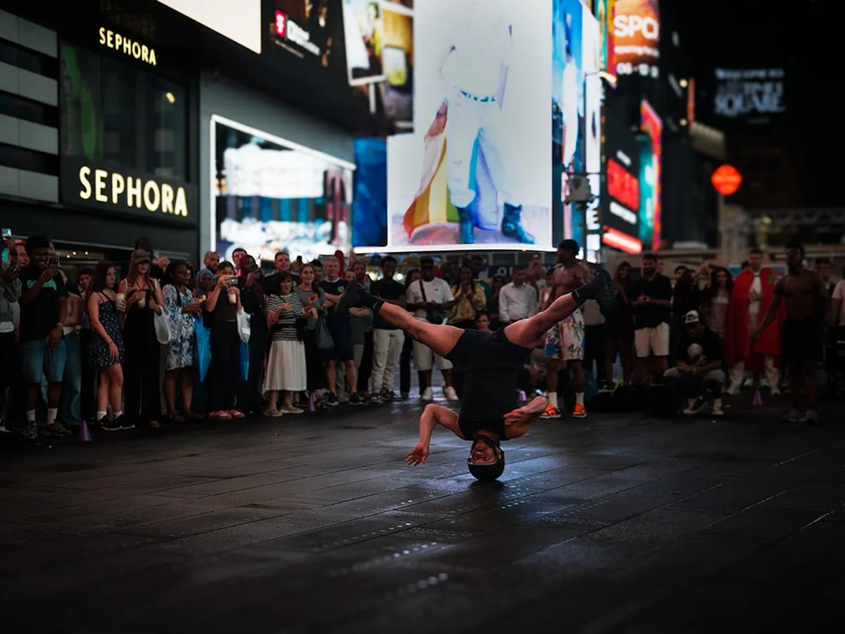 Breakdancer performing headspin with legs extended in air in Times Square with Sephora and billboards behind