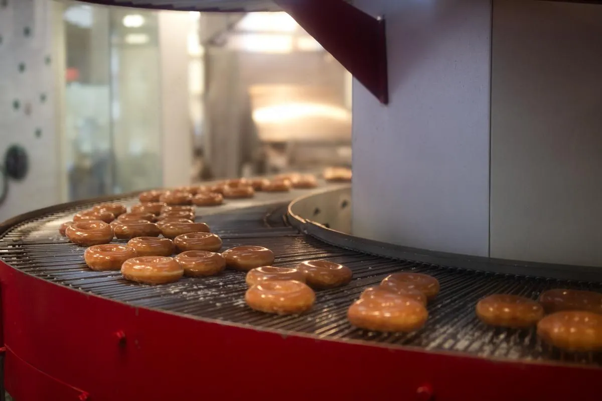 Fresh glazed donuts rolling on red conveyor belt in donut shop kitchen