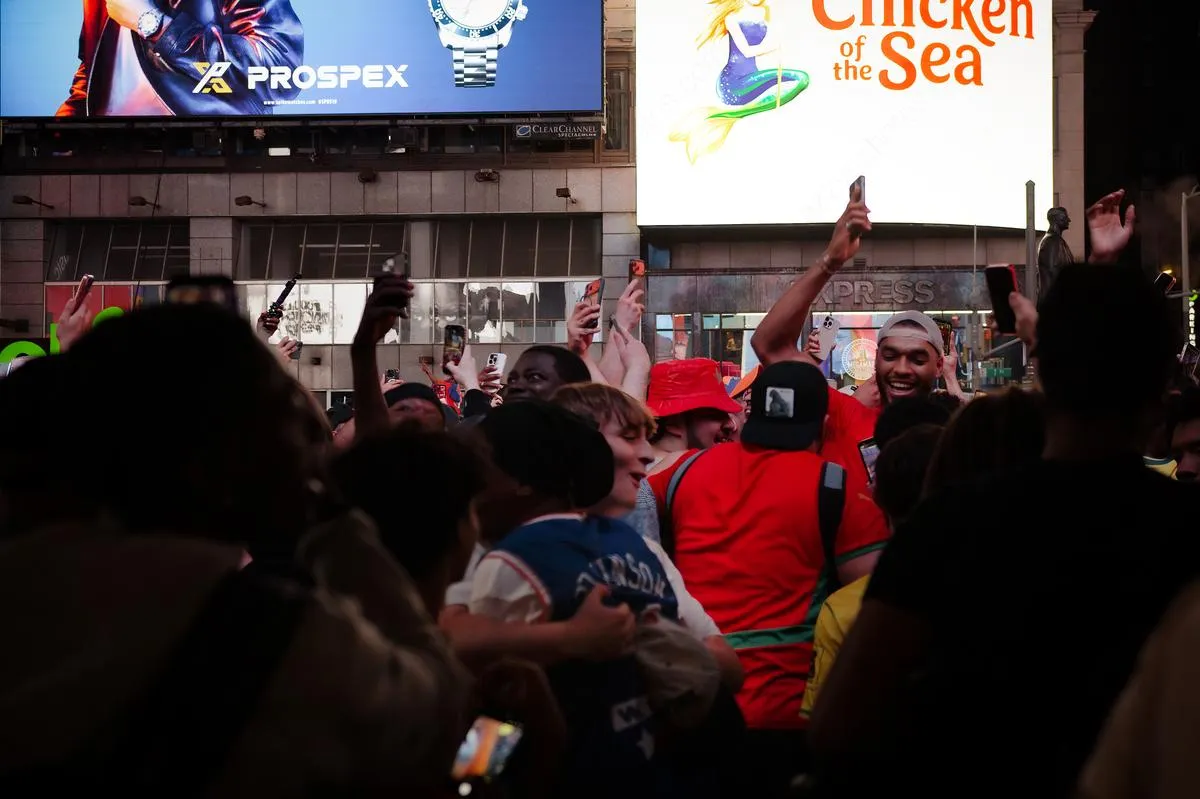 Ecstatic crowd of Morocco fans with arms raised and phones held high, celebrating under Times Square billboards at night
